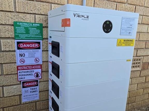 A white battery storage system against a brick wall