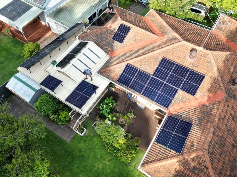 A man stands on a roof looking down on a solar panel