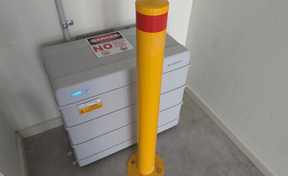 A Sungrow battery installed behind a yellow bollard.